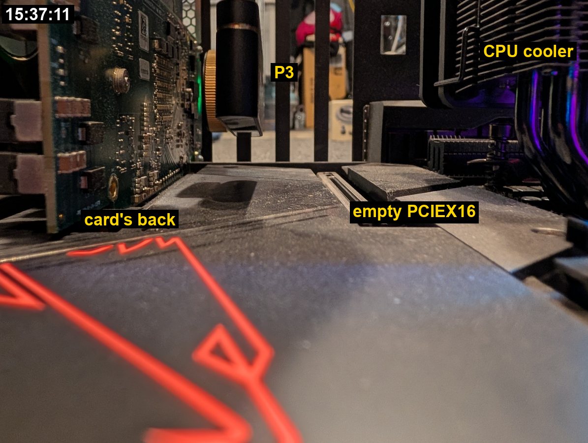 Low view across the motherboard between the card and the CPU cooler: the card's component-covered back on the left, the P3 hanging by its cable, the empty PCIe slot and the cooler on the right.